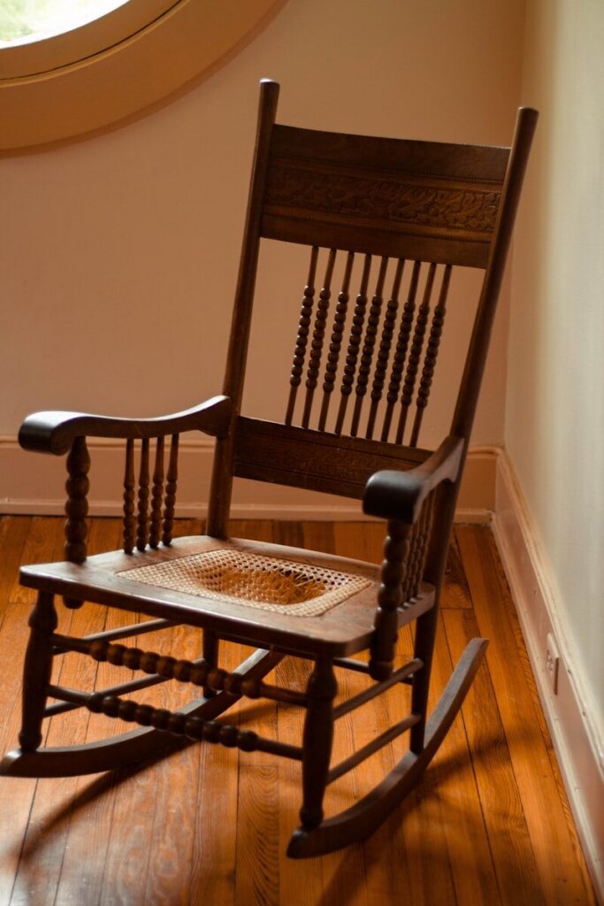 A wooden rocking chair rests by a window.